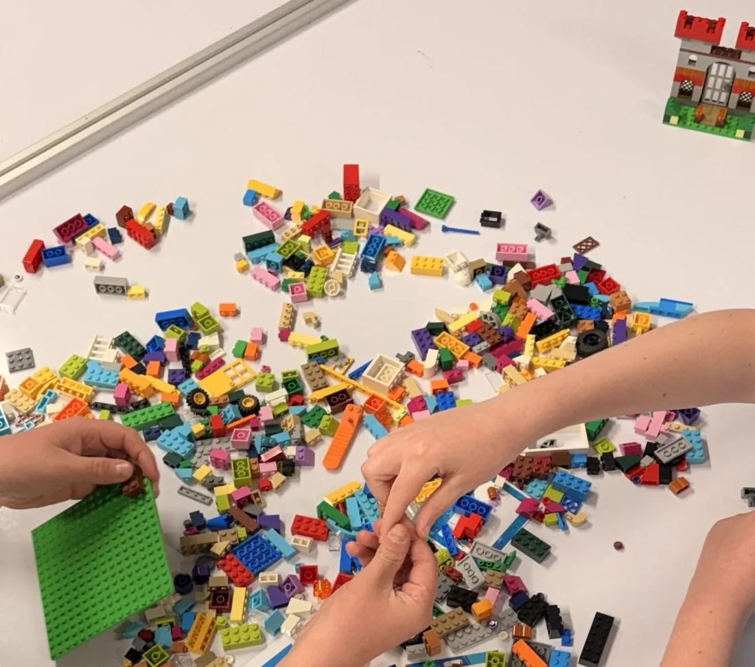 Two children's hands building together with LEGO® bricks on a table at a LEGO® Based Therapy Group